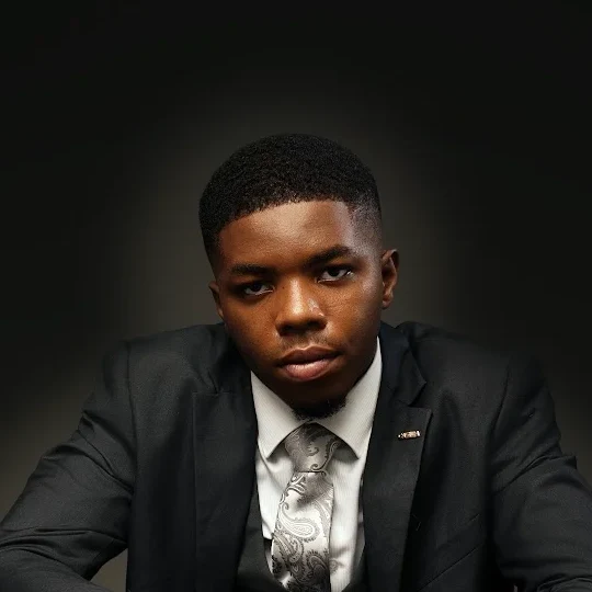 Portrait of Israel Nnaji in a dark suit seated at a table